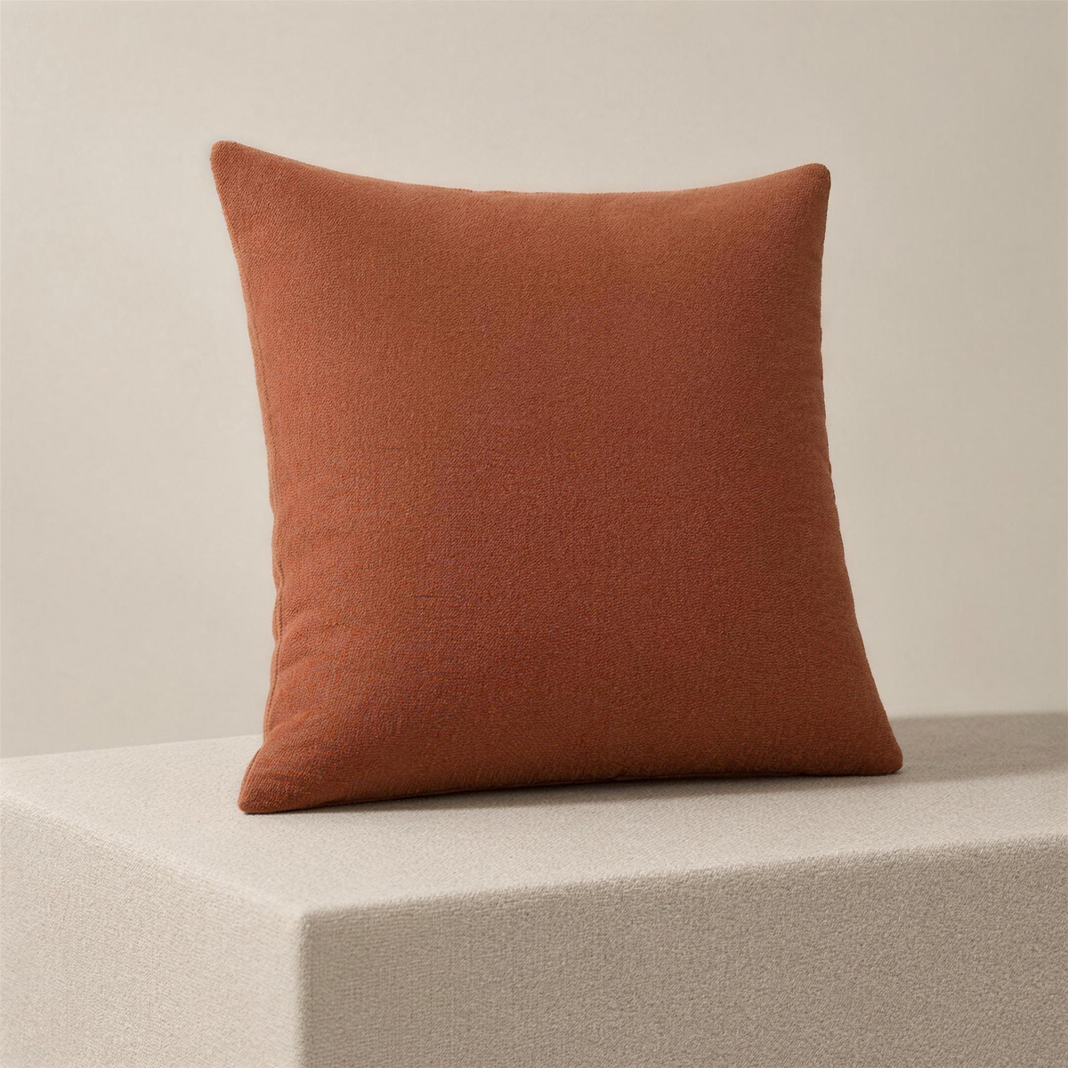 The Case in clay, a square cushion cover in one flat terracotta colour, standing upright on a plinth.