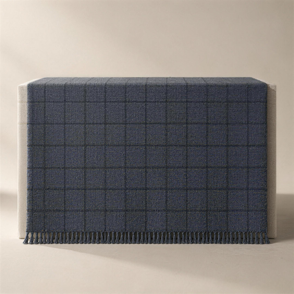 The Woven in slate, draped face-up over a plinth, the windowpane grid woven into the cloth in a darker charcoal and a knotted fringe along the lower edge.