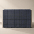 The Woven in slate, draped face-up over a plinth, the windowpane grid woven into the cloth in a darker charcoal and a knotted fringe along the lower edge.