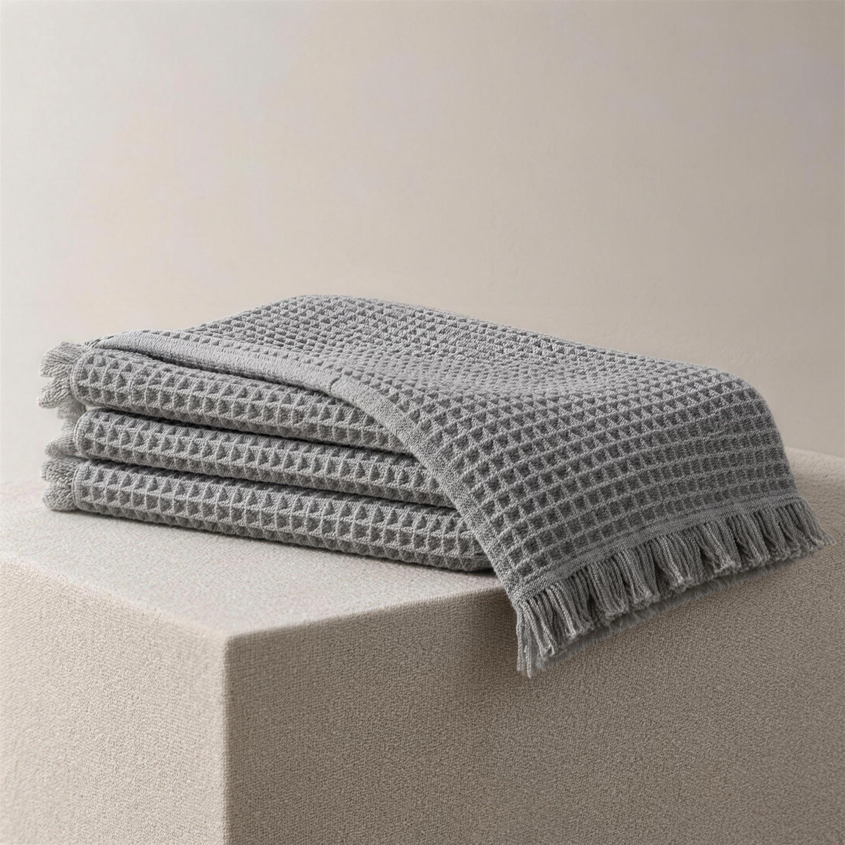 The Waffle in ash, folded on a plinth with the top layer fallen open, showing the deep waffle pockets and the fringed end.