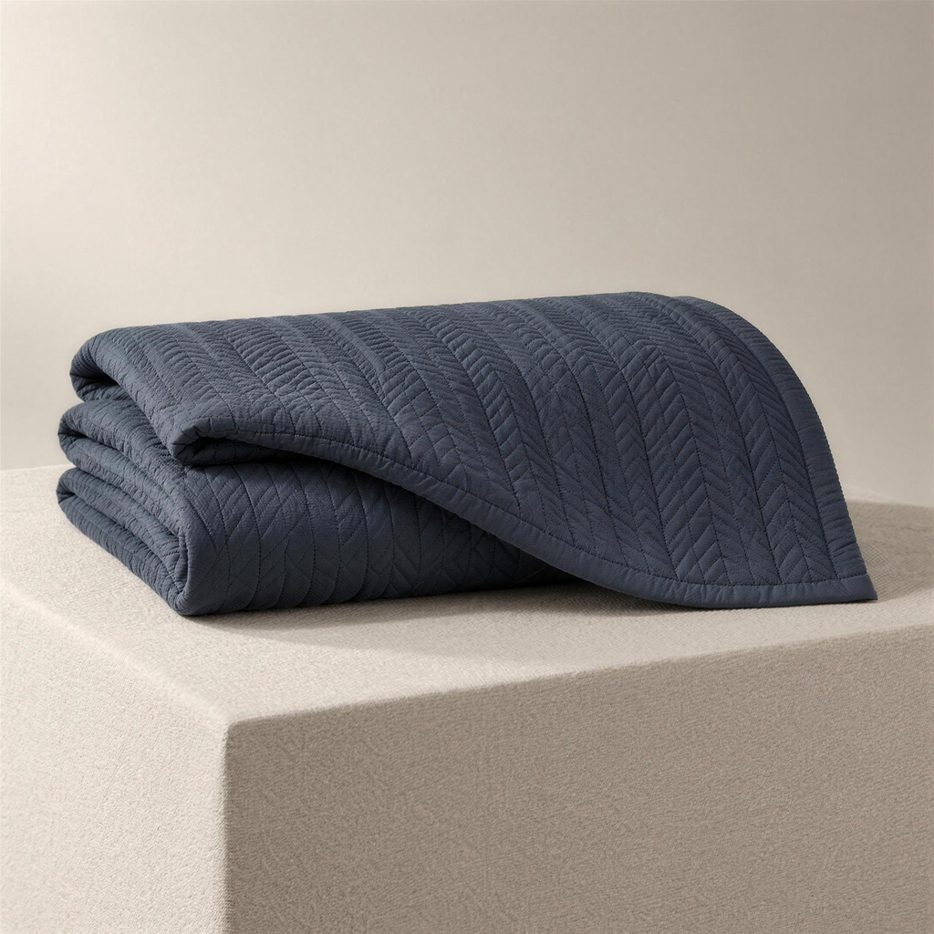 The Quilt in slate, folded on a plinth, narrow chevron-stitched columns catching the light.
