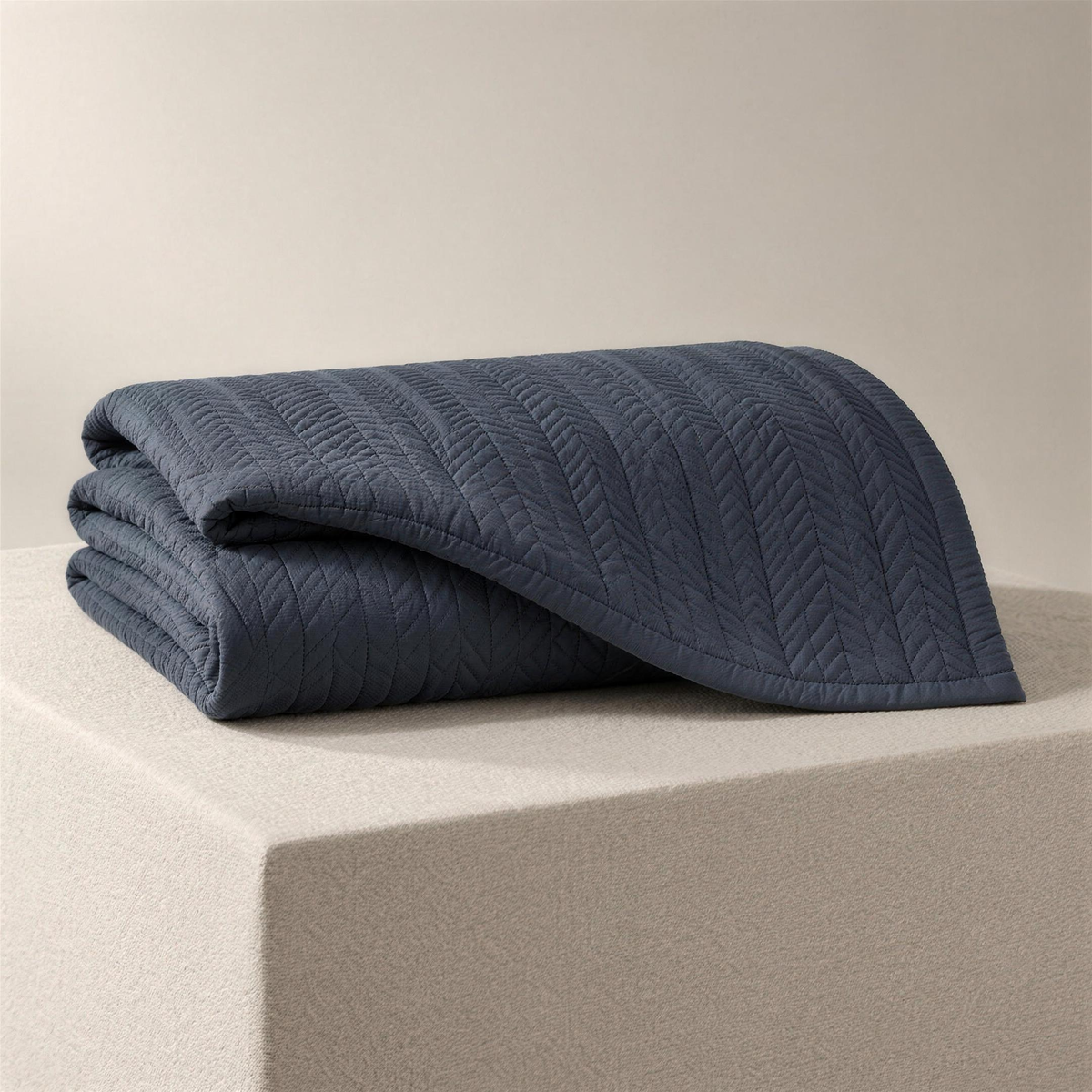 The Quilt in slate, folded on a plinth, narrow chevron-stitched columns catching the light.